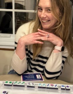 Happy Mahjong student smiling proudly at the game table with tiles arranged in front of her.